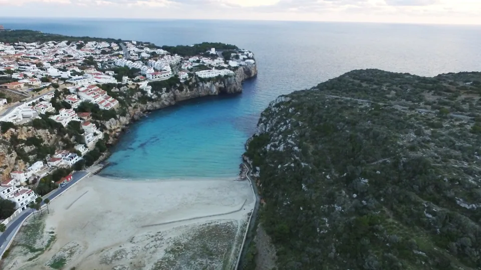 Enseada de Cala en Porter com praia e edifícios brancos junto à encosta.