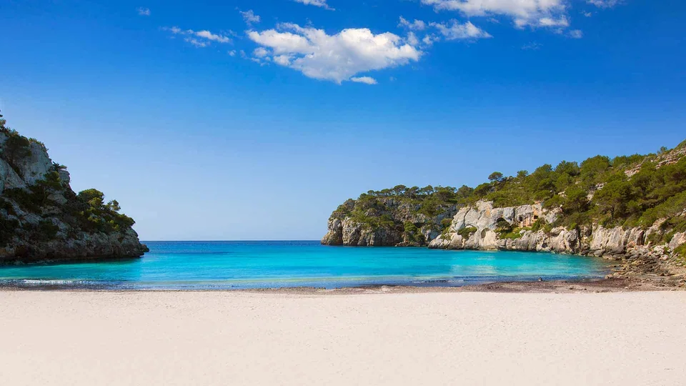 Cala Macarella, com areal claro, falésias e pinheiros nas encostas.