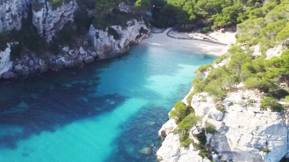 Pequena enseada de Cala Macarelleta, com água turquesa, rocha e pinheiros.