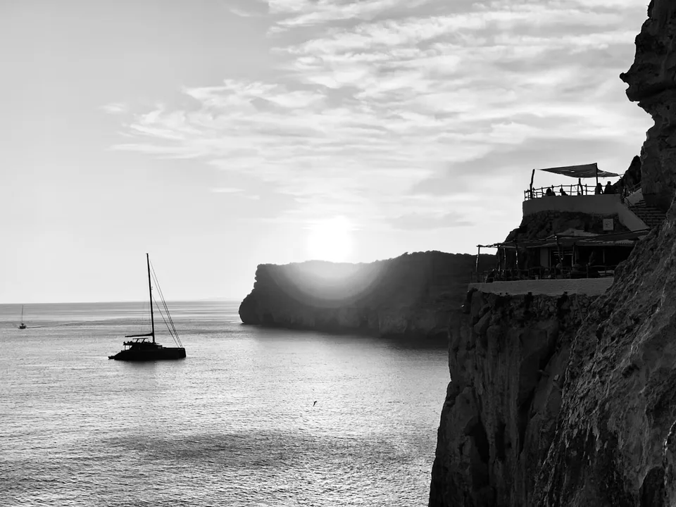Terraços da Cova d’en Xoroi na falésia sobre o mar, numa fotografia a preto e branco.