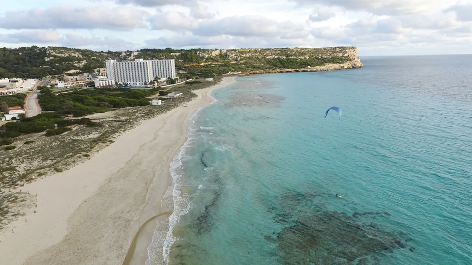 O longo areal de Son Bou junto ao mar, com edifícios visíveis ao fundo.